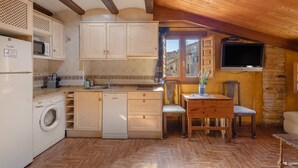 A compact kitchen with wooden cabinets, a washing machine, a sink, and a dining area with a table and chairs.
