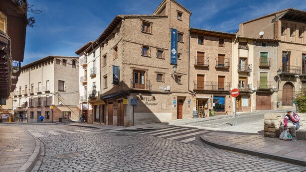 A cobblestone street with historic buildings, a 'Pinar' sign, and a 'Tica' sign.