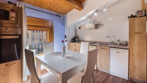 Een moderne keuken met houten kastjes, een inbouwoven en een eethoek met een tafel en stoelen.