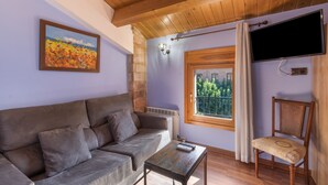 Een kamer met een bank, een tafel, een aan de muur bevestigde televisie en een raam met uitzicht.