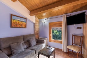 Ein Zimmer mit einer Couch, einem Tisch, einem an der Wand montierten Fernseher und einem Fenster mit Blick.