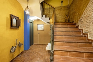 Eine Treppe mit Holzbalken führt zu einer zweiten Etage, eine Wandleuchte, eine blaue Wand und eine Tür mit einem Schild.
