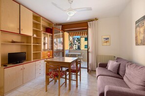 Una sala de estar con sofá, televisor, mesa de comedor con sillas, armarios de madera y ventilador de techo.