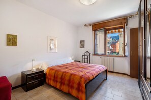 Un dormitorio con cama, mesita de noche, ventana con vistas y radiador.