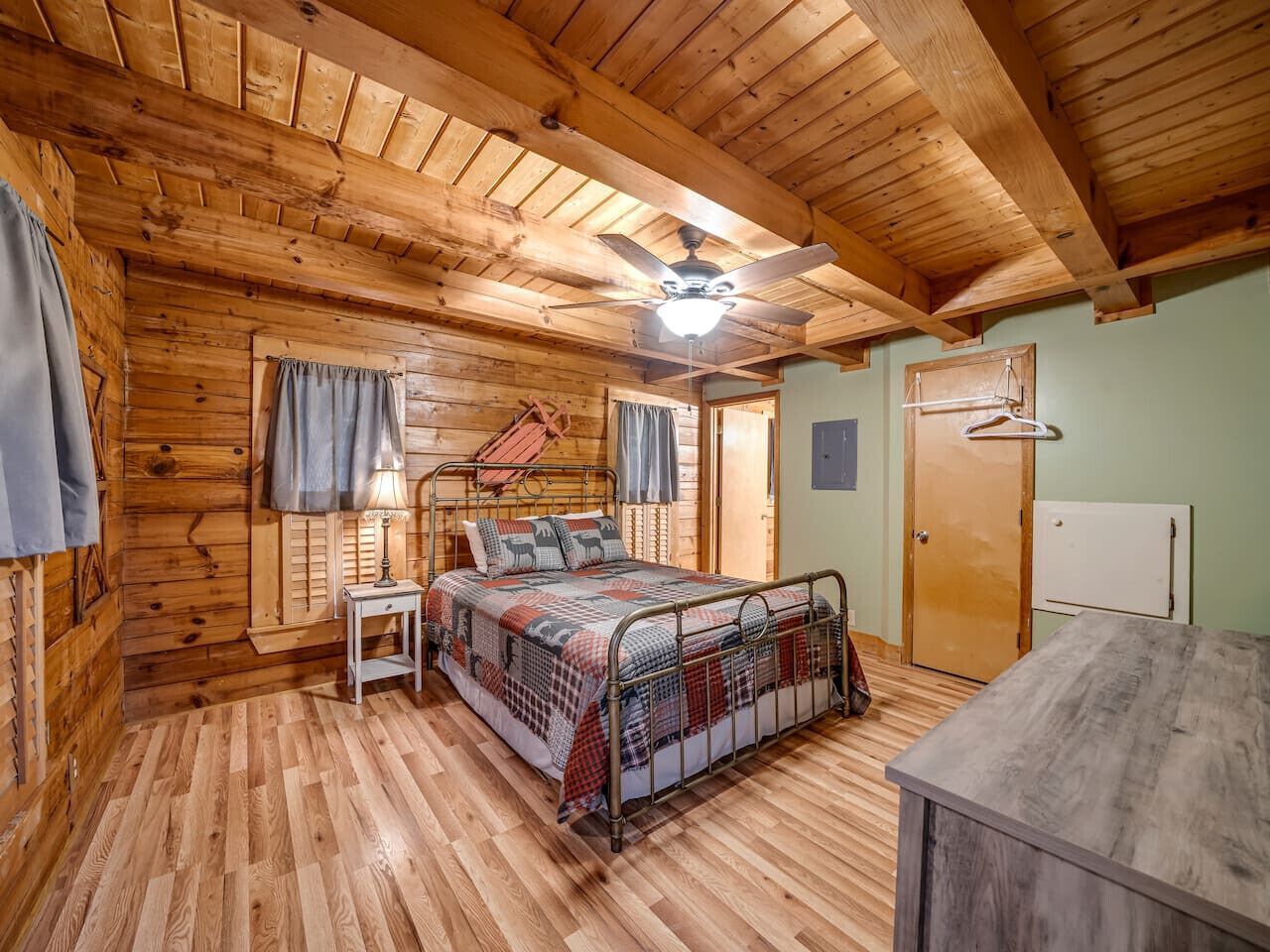 A cozy cabin-style bedroom with a wooden ceiling, a bed with a metal frame, a small bedside table, and a wardrobe.
