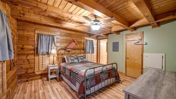 A cozy cabin-style bedroom with a wooden ceiling, a bed with a metal frame, a small bedside table, and a wardrobe.