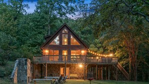 Une cabane en bois dotée d’un balcon, de fondations en pierre et illuminée de guirlandes lumineuses.