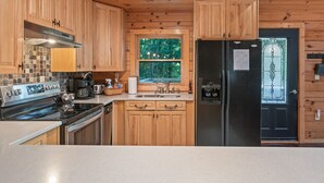 Une cuisine avec des meubles en bois, une cuisinière en acier inoxydable, un réfrigérateur et une fenêtre donnant sur les arbres.
