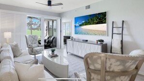 Een moderne woonkamer met een bank, fauteuils, een salontafel en een tv die aan de muur bevestigd is boven een console tafel met een patroon.