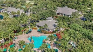 Luchtbeeld van een resort met een centraal gelegen zwembad, omringd door palmbomen en een golfbaan.