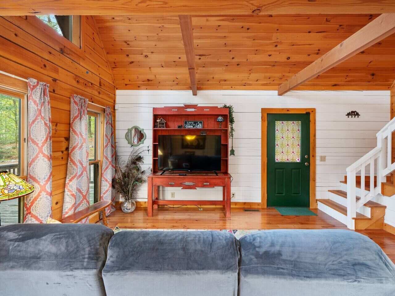 Interior acogedor de una cabaña con techo de madera, un televisor sobre un mueble de madera, una puerta verde y una escalera.