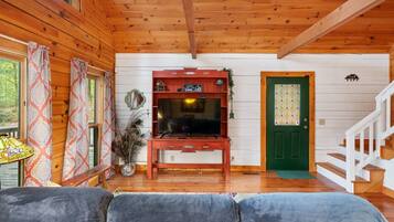 Interior acogedor de una cabaña con techo de madera, un televisor sobre un mueble de madera, una puerta verde y una escalera.