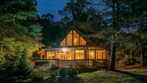 Une cabane dotée d’une terrasse en bois, de grandes fenêtres et d’un porche.