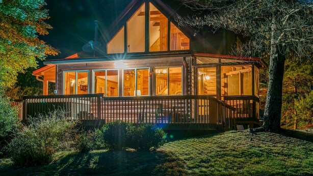 Une maison en bois à deux étages, dotée de grandes fenêtres et d’un porche abrité.