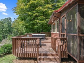 Une terrasse en bois avec un jacuzzi, un espace salon couvert et une vue sur une zone boisée.