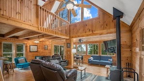 Une cabane spacieuse avec une chambre en mezzanine, un salon doté de canapés en cuir, un coin repas et un poêle à bois.