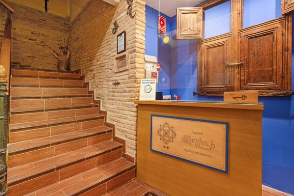 A hotel reception desk with a wooden counter, a sign indicating room availability, and a staircase with wooden steps.