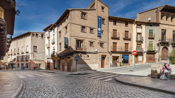 A cobblestone street with historic buildings, a 'Pinar' sign, and a 'Tica' sign.