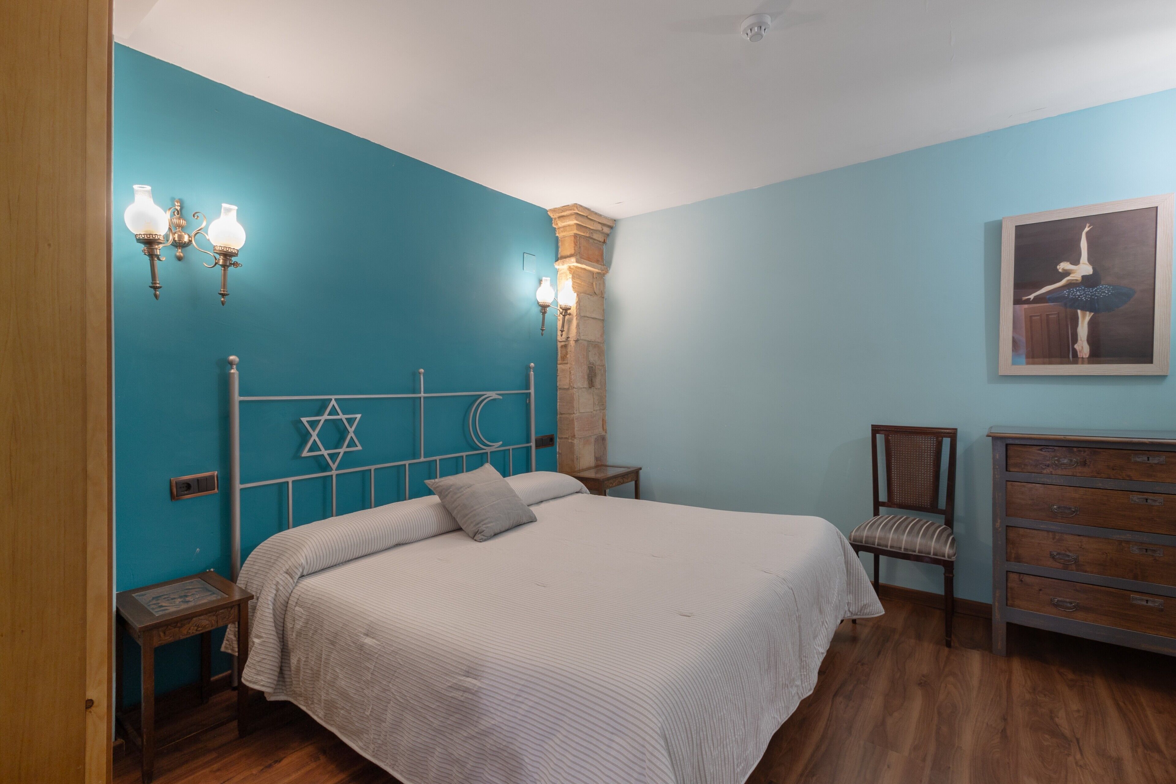 Een slaapkamer met een bed, een dressoir, een stoel en een wandlamp.