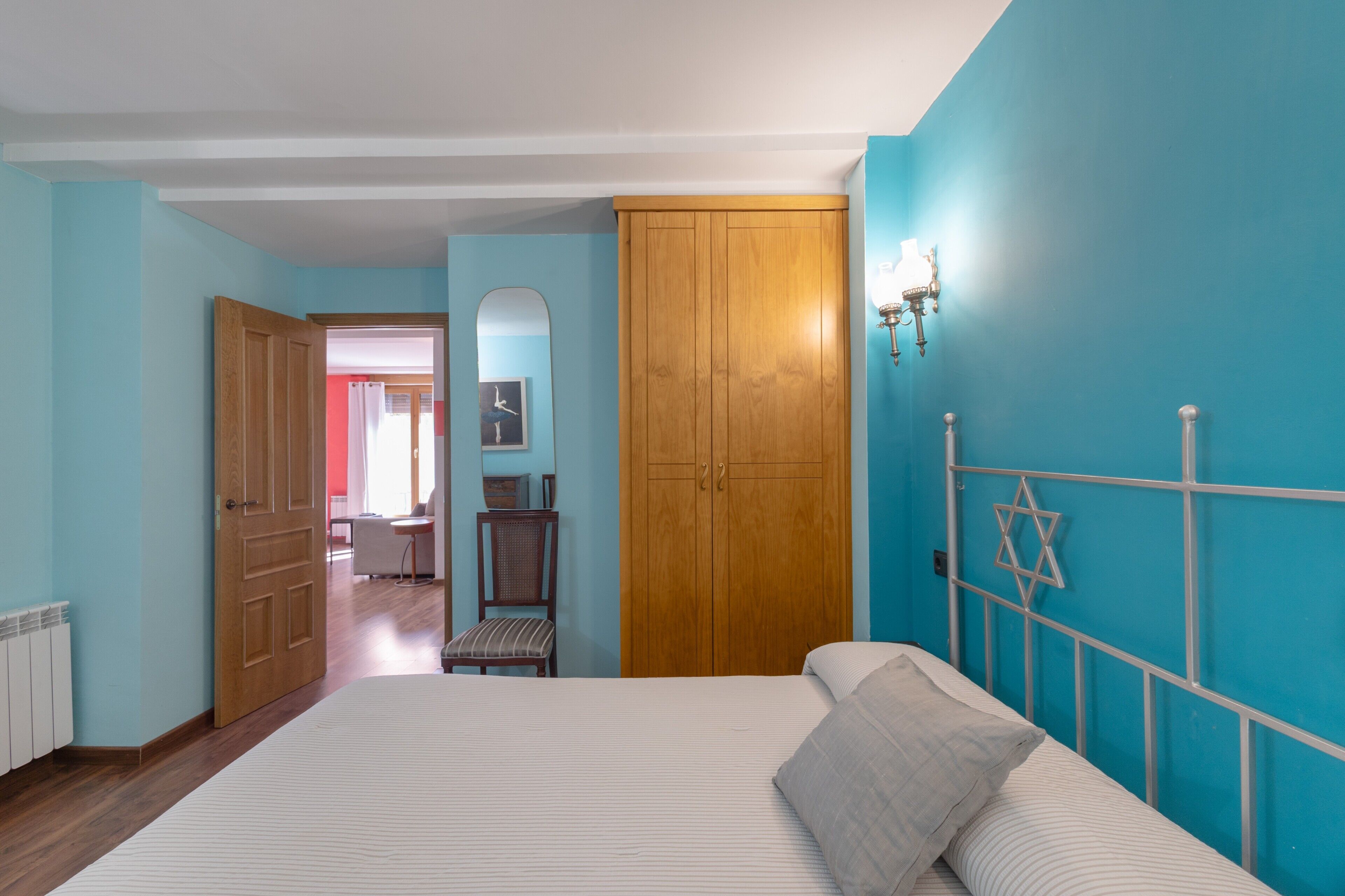 Une chambre à coucher comprenant un lit, une armoire en bois, une chaise et un luminaire fixé au mur.