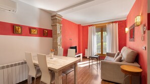 A room with a dining table, chairs, a sofa, a small round table, a stone pillar, a TV, and a window with curtains.