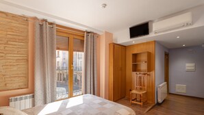 A bedroom with a bed, a wooden chair, a wardrobe, a television, and an air conditioning unit.