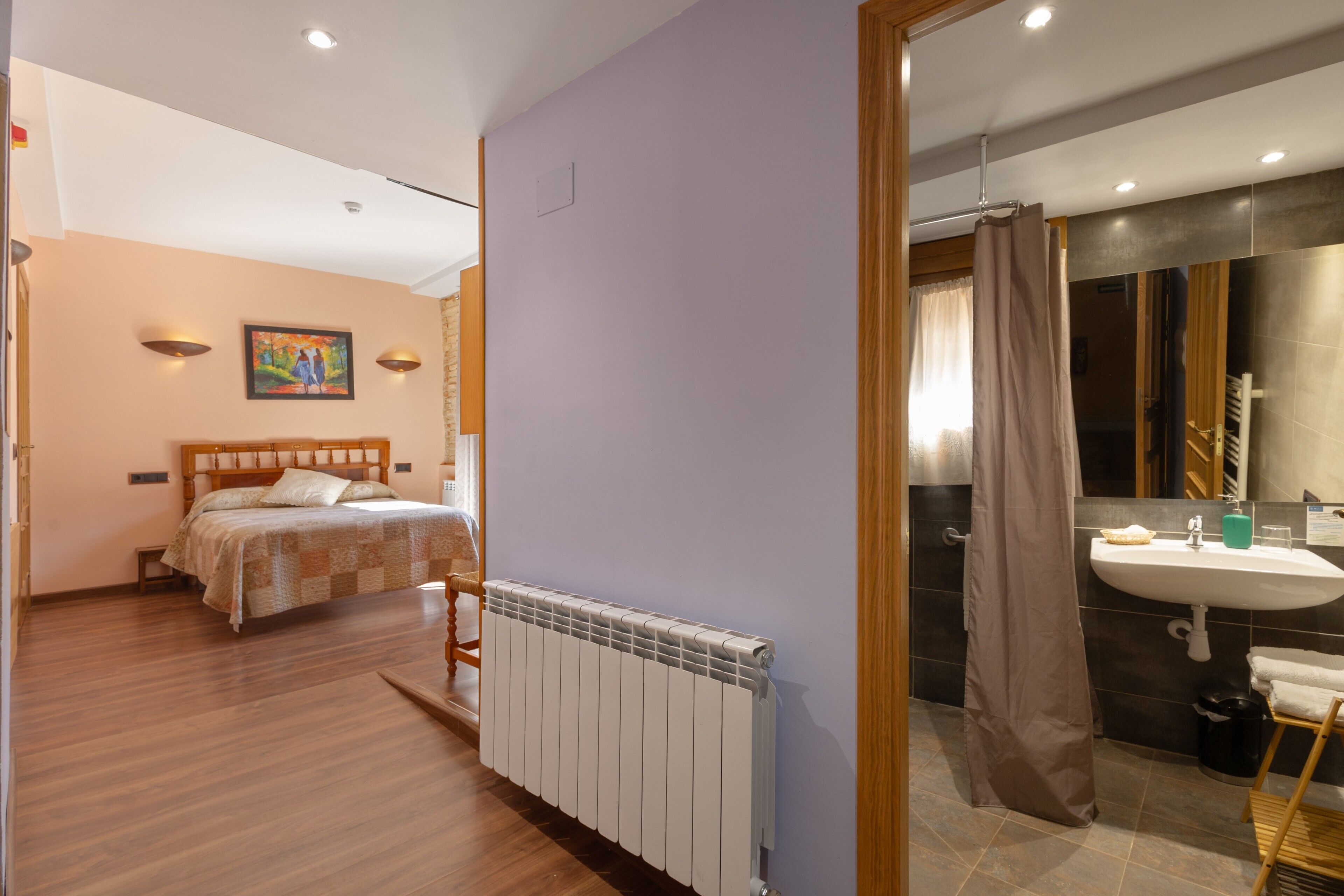A bedroom with a bed, a radiator, and a bathroom with a sink and shower.
