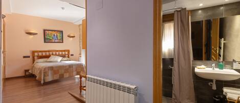 A bedroom with a bed, a radiator, and a bathroom with a sink and shower.