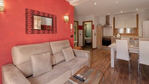 A living room with a sofa and a coffee table, a kitchen with a dining area, and a red accent wall.