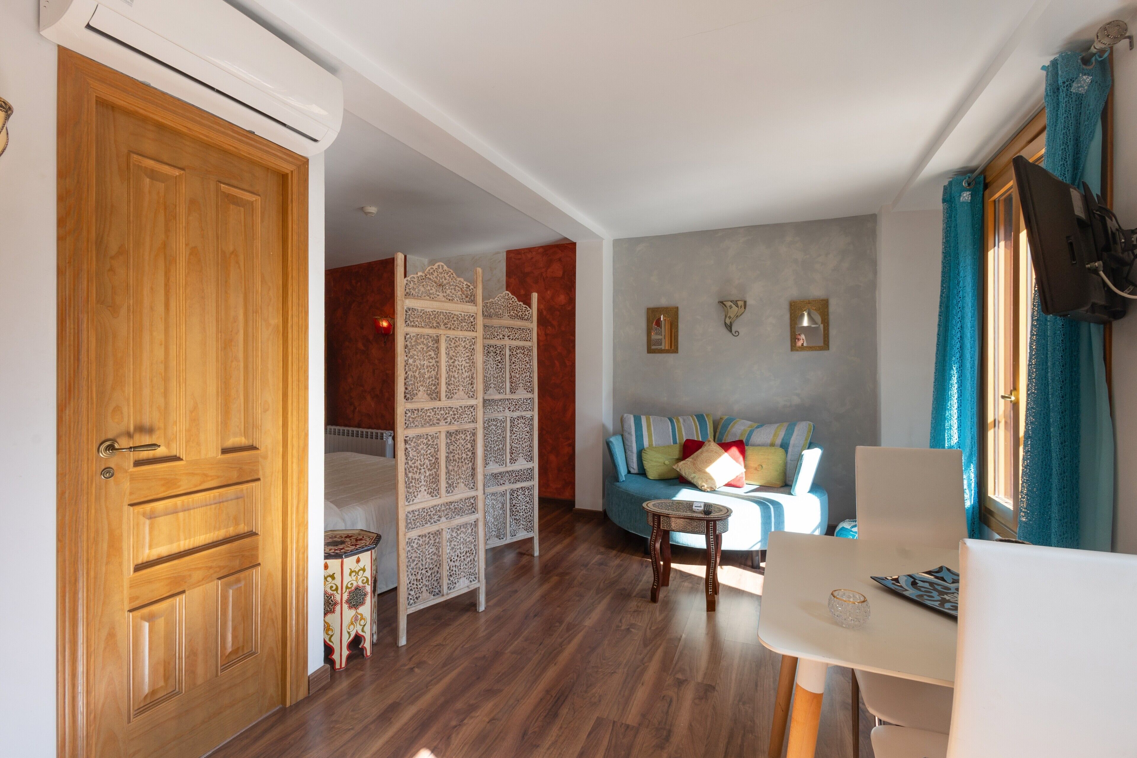 Een kamer met een houten deur, een bed, een blauwe bank, een kleine tafel en een televisie.