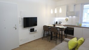 A modern kitchen with a dining area, a flat-screen TV mounted on the wall, and a sofa with bright yellow cushions. - Comfortable apartment in the center of Arenzano, a few steps from the sea (Arenzano)