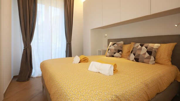 A neatly made bed with a yellow patterned bedspread, two pillows with a geometric design, and a pair of folded towels. - Comfortable apartment in the center of Arenzano, a few steps from the sea (Arenzano)
