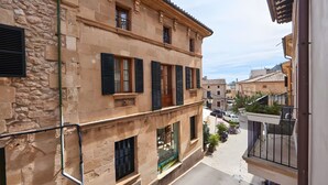 Un edificio de varios pisos con paredes de piedra, ventanas con contraventanas y un balcón con maceta.