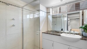 Een moderne badkamer met een douchecabine van glas, een witte wastafel en een grote spiegel.