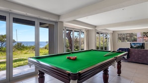 Une table de billard placée de manière à offrir une vue dégagée sur la mer grâce à de grandes fenêtres.