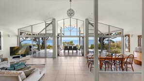 Amplia sala de estar con un televisor grande, una mesa de comedor con sillas y vista al océano.
