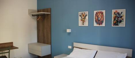 A hotel room with a bed, a desk, a chair, and artwork on the wall.
