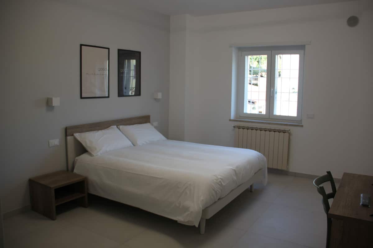 A bedroom with a bed, a nightstand, a window, and a chair.