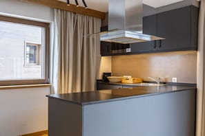 A modern kitchen with a central island, dark cabinetry, and a window with curtains.