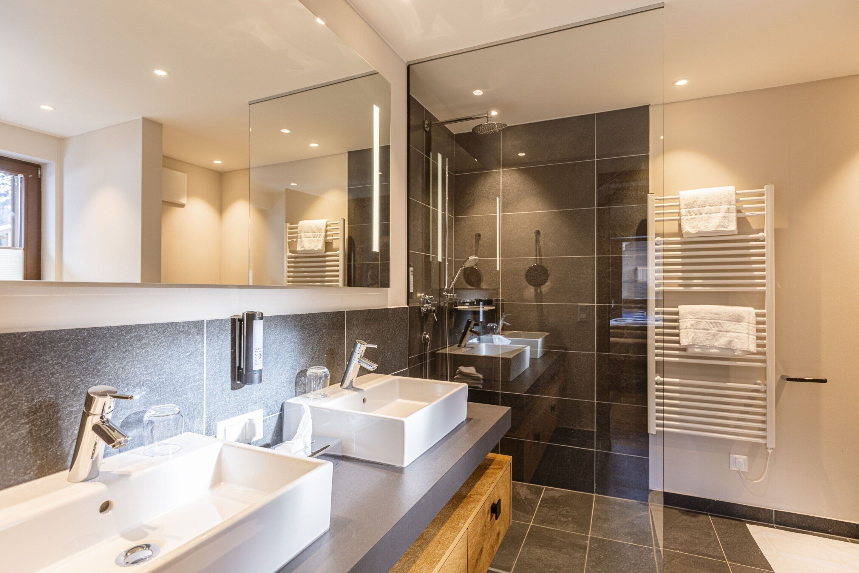 Een moderne badkamer met drie wastafels, een grote spiegel en een douchecabine met glazen wanden.