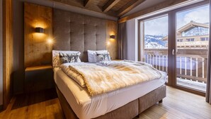 Ein Schlafzimmer mit einem großen Bett, Holzbalkendecke, einer Schiebeglastür zu einem Balkon und zwei Wandleuchten.