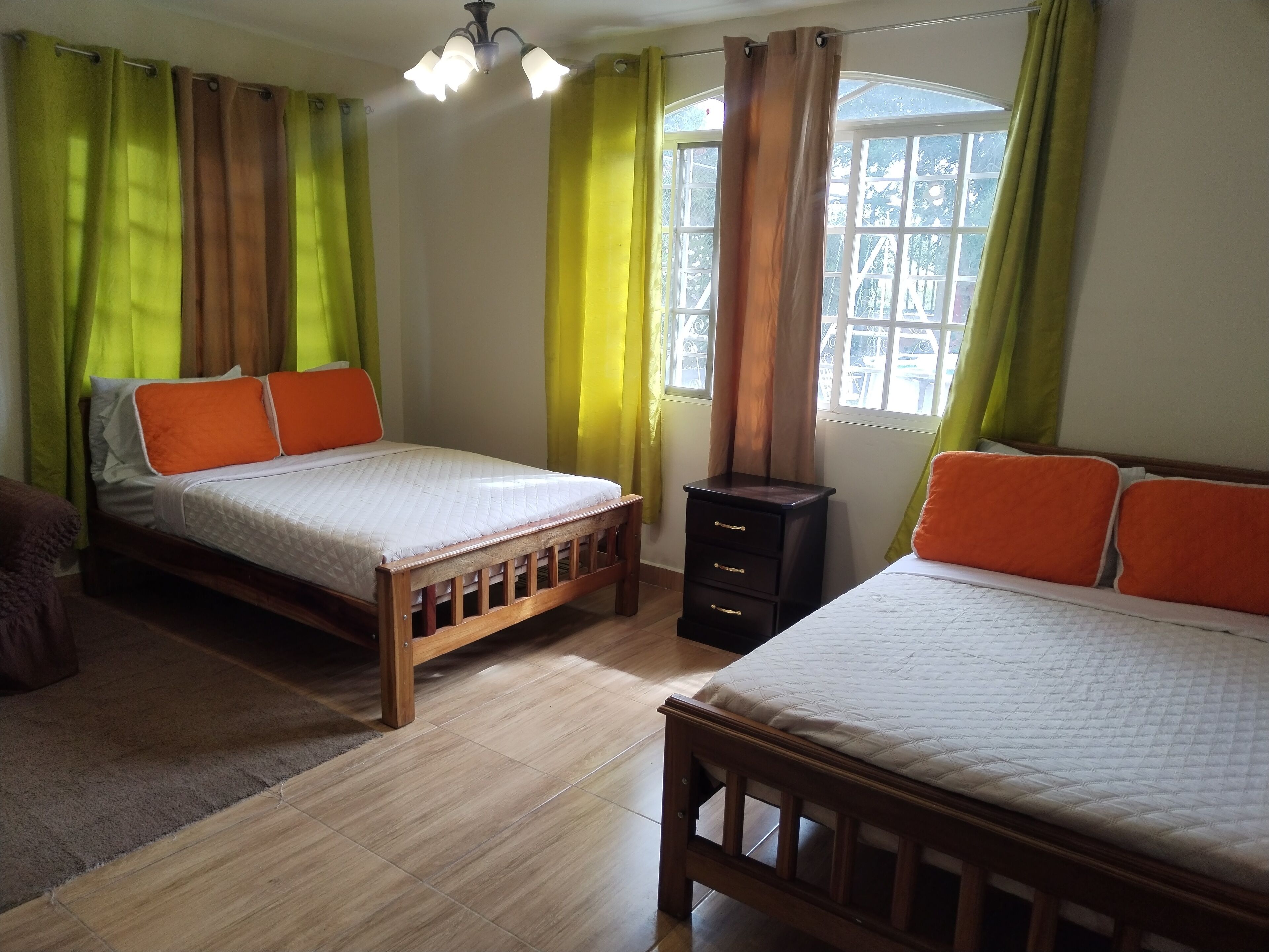 Ein Zimmer mit zwei Holzbettgestellen, einer kleinen, dunkelbraunen Kommode und einem Fenster mit Vorhängen.