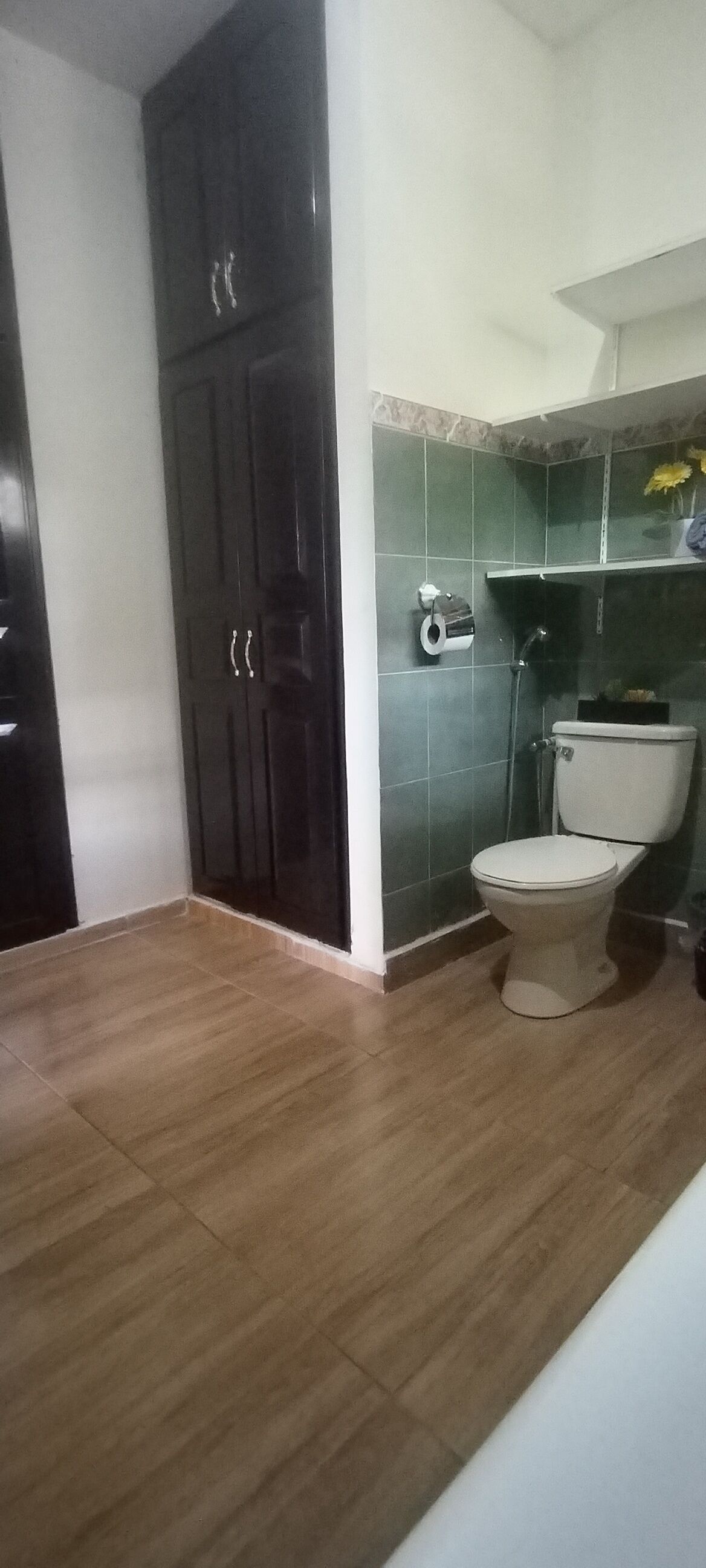 Une salle de bain avec des toilettes, une armoire en bois foncé, des murs carrelés et un plancher en bois.
