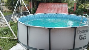Una piscina elevada con escalera, rodeada de follaje y un columpio.