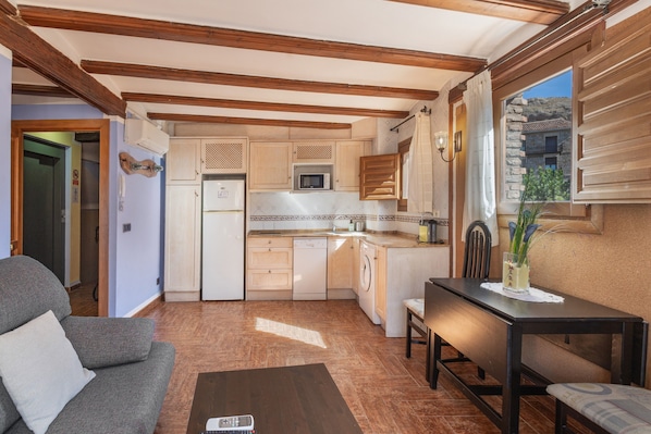 A compact kitchen with wooden beams, a dining area with a table and chairs, and a sofa.