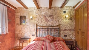 Une chambre avec un mur en pierre, un cadre de lit en bois, deux tables de chevet et une petite table de nuit.