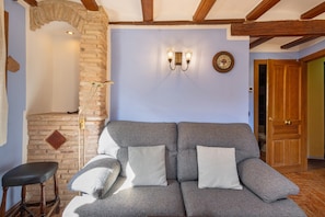 A living room with a sofa, two wall-mounted lights, a clock, and a wooden door.