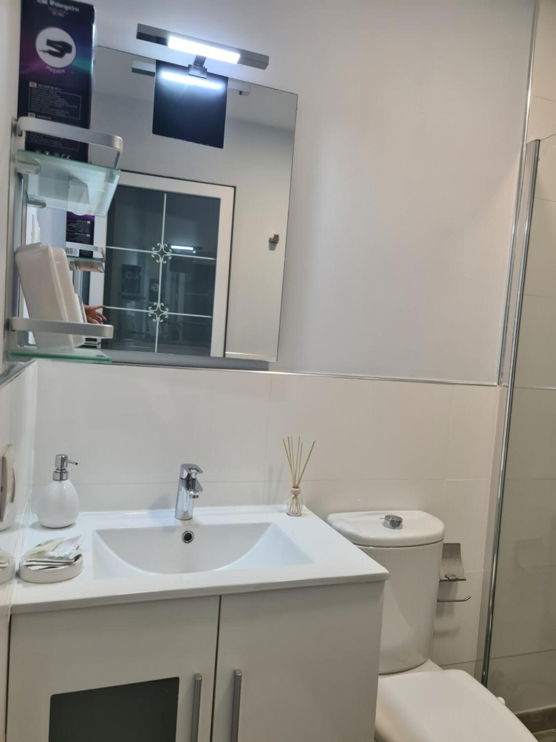 Un baño con lavamanos, espejo y retrete blancos.