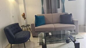 Una sala de estar con un sofá, una silla, una mesita de vidrio y un florero con flores.