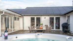 A backyard with a hot tub, a dining table with chairs, and a barbecue grill. - Elegant Blavand Getaway- By Traum Ferienwohnungen (Blavand)